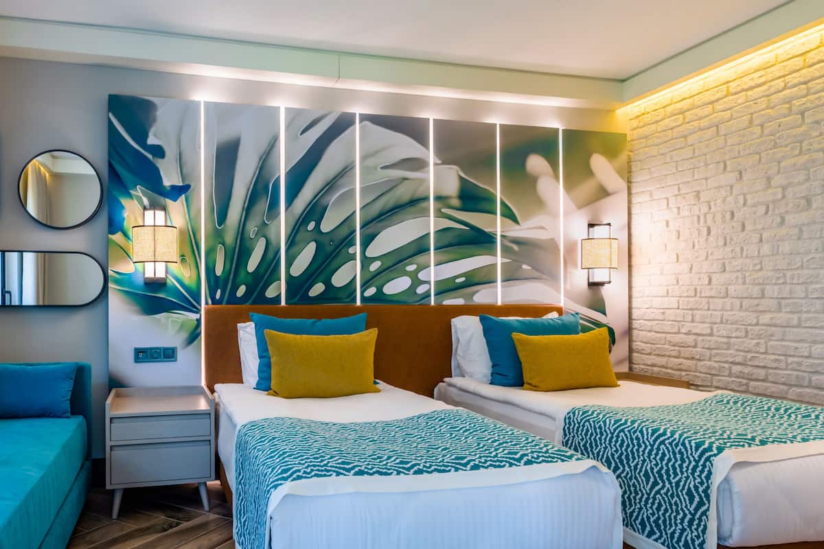 A hotel room with two beds, a nightstand, a mirror, and a wall with a leaf pattern.