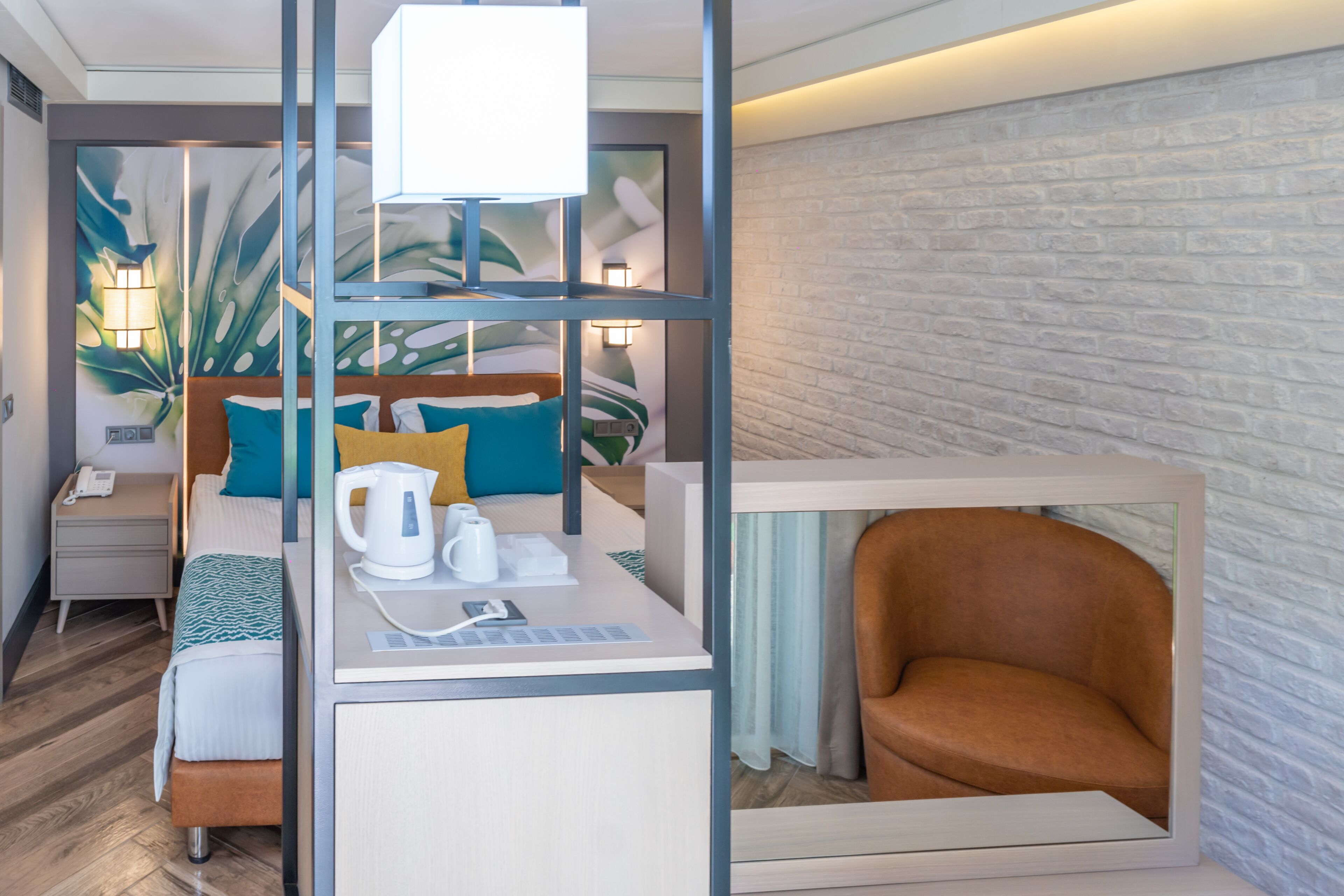 Une chambre d’hôtel moderne équipée d’un lit, d’un bureau avec une bouilloire, d’une chaise et d’un grand miroir.