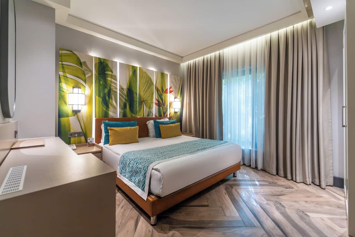A hotel room with a bed, bedside table, lamp, and a large window with curtains.