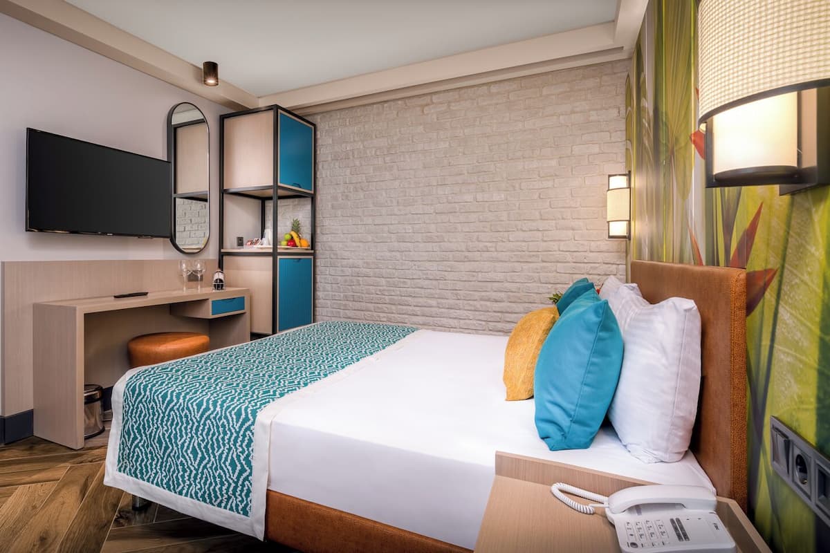 A hotel room with a bed, a desk, a TV, and a phone.