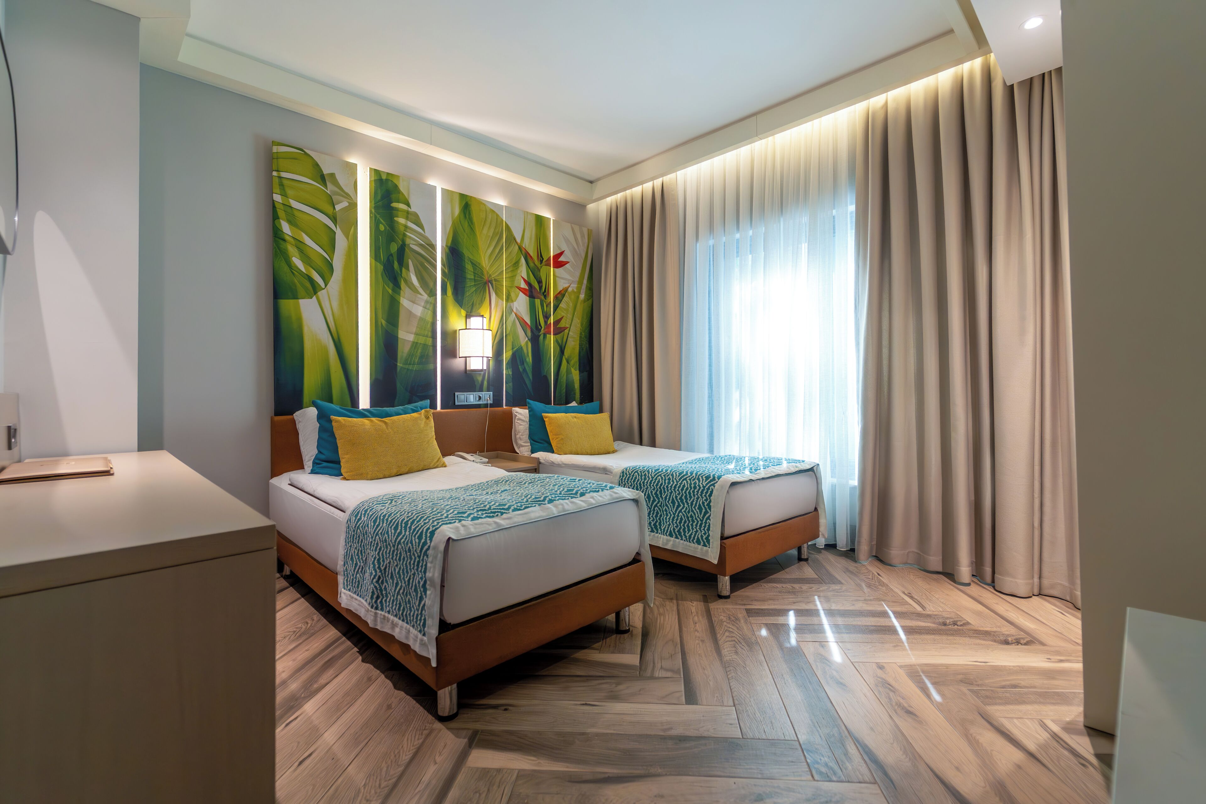 Una habitación de hotel con dos camas, un escritorio y un amplio ventanal con cortinas.
