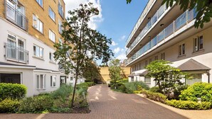 A residential building with multiple floors, balconies, and a paved pathway lined with greenery.