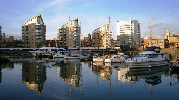 A marina with several boats docked, surrounded by modern buildings with balconies and large windows.