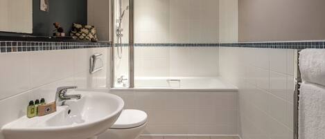 A modern bathroom with a white sink, toilet, and bathtub. There is a shower area with a glass door. The walls are tiled, and there is a towel rack on the right.