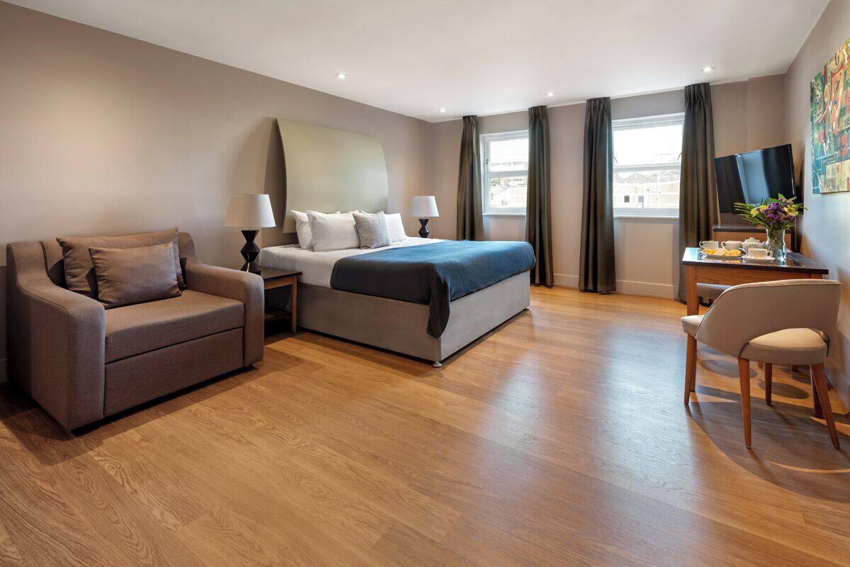 Ein modernes Hotelzimmer mit Bett, Sofa, Schreibtisch und Stuhl sowie einem Fernseher.