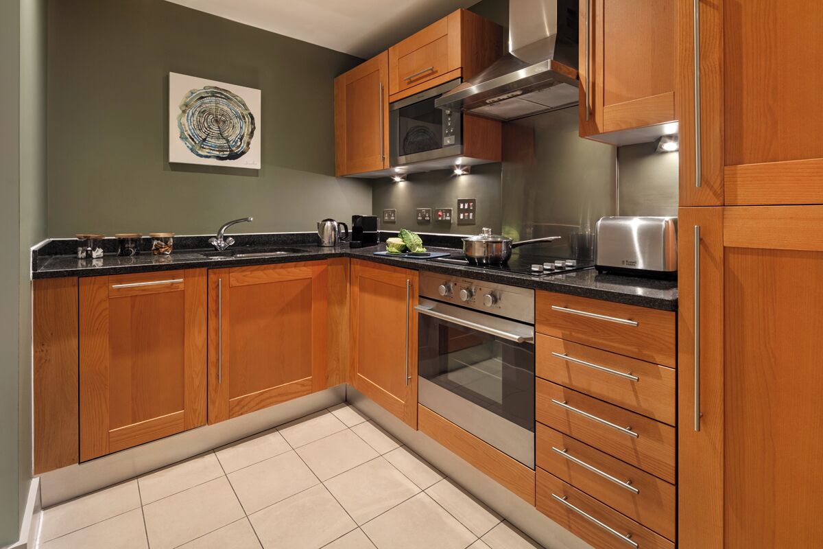 A modern kitchen with wooden cabinets, stainless steel appliances, and a tiled floor.