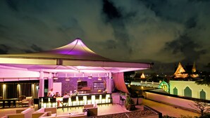 Uma área de bar ao ar livre com espaço de estar coberto, balcão de bar e vista para um templo ao fundo.