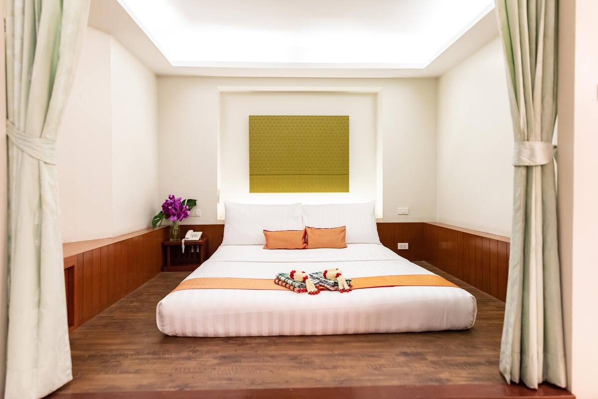 Quarto de hotel com uma cama grande, uma mesa de cabeceira com um vaso de flores e uma janela com vista.