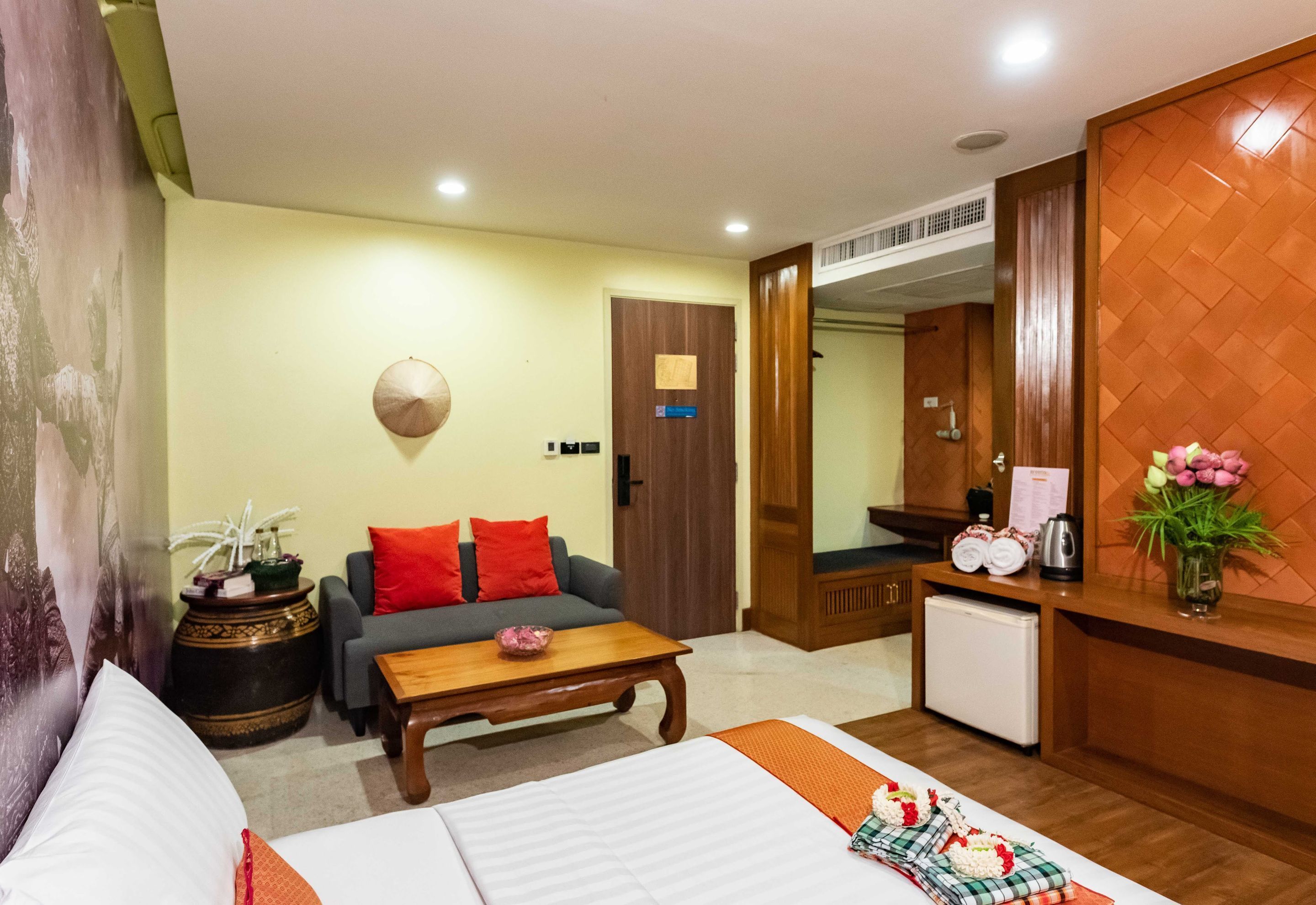 A hotel room with a bed, a sofa, a coffee table, a small table with a vase, and a kitchenette.