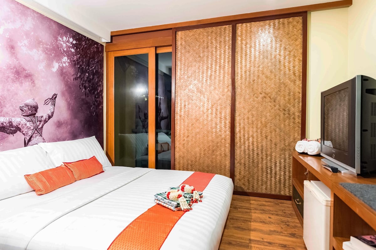 Quarto de hotel com uma cama, televisão, guarda-roupa e uma parede com um mural.