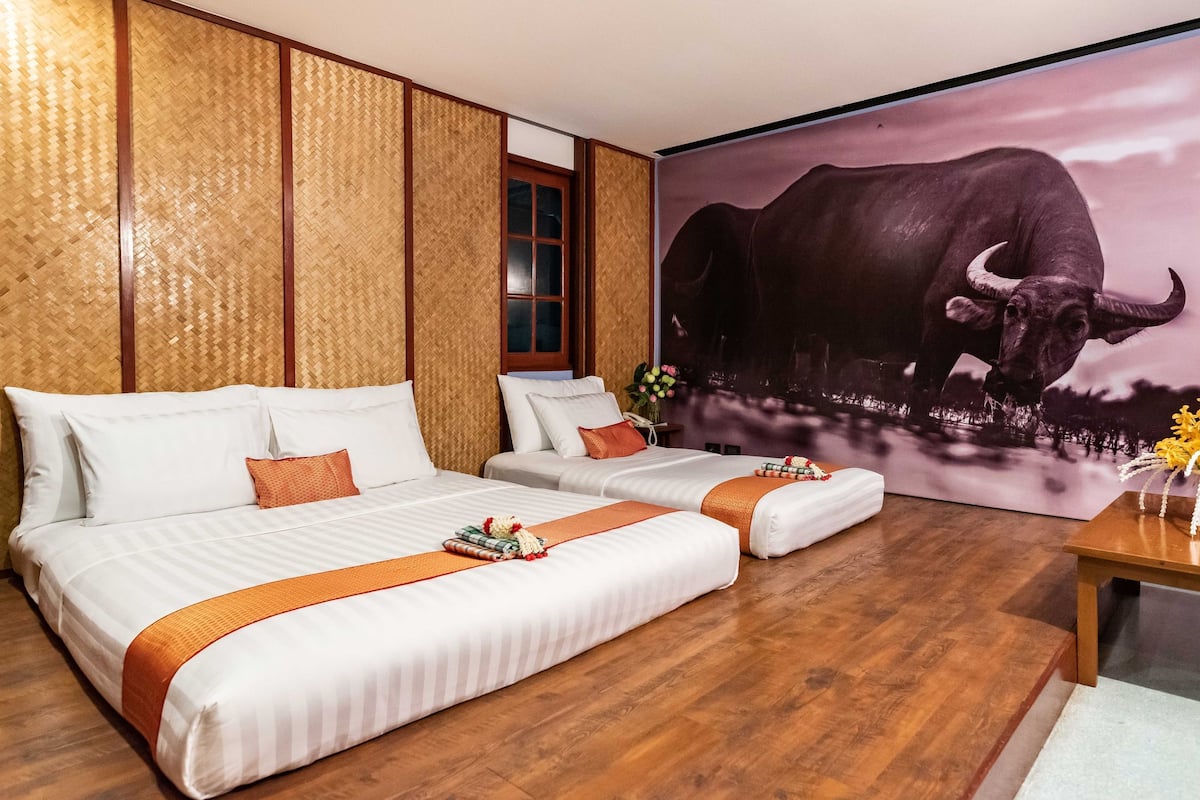 Quarto de hotel com duas camas, painéis de madeira, um grande mural de um búfalo e piso de madeira.