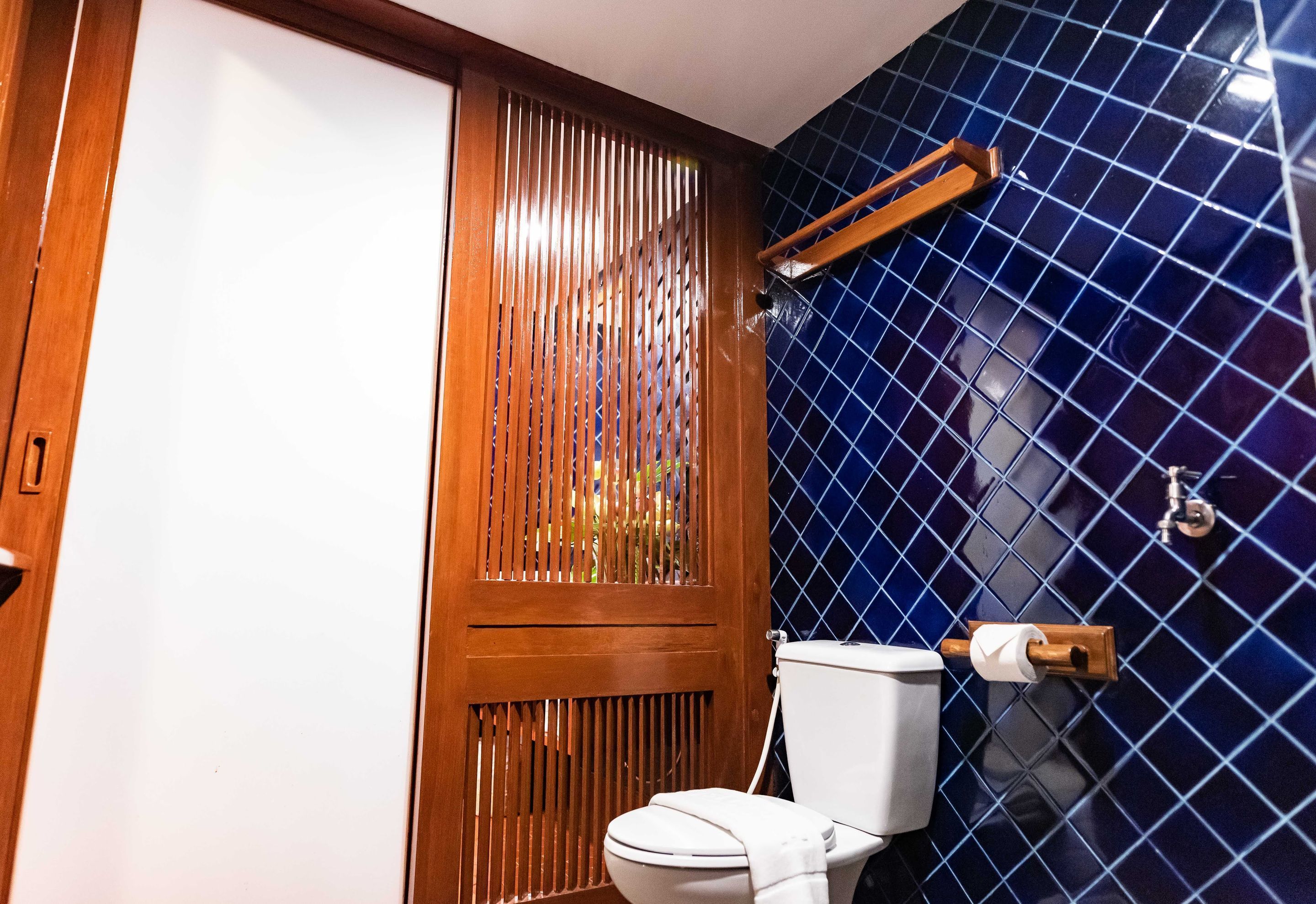Un baño con puerta de madera, inodoro y pared con azulejos azules.