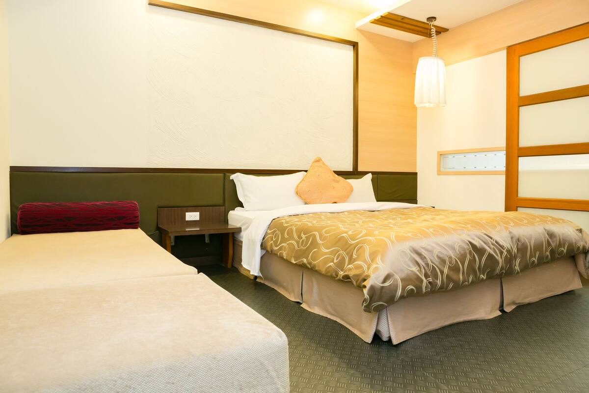 Une chambre d’hôtel avec deux lits, une table de chevet, une lampe et un luminaire fixé au mur.