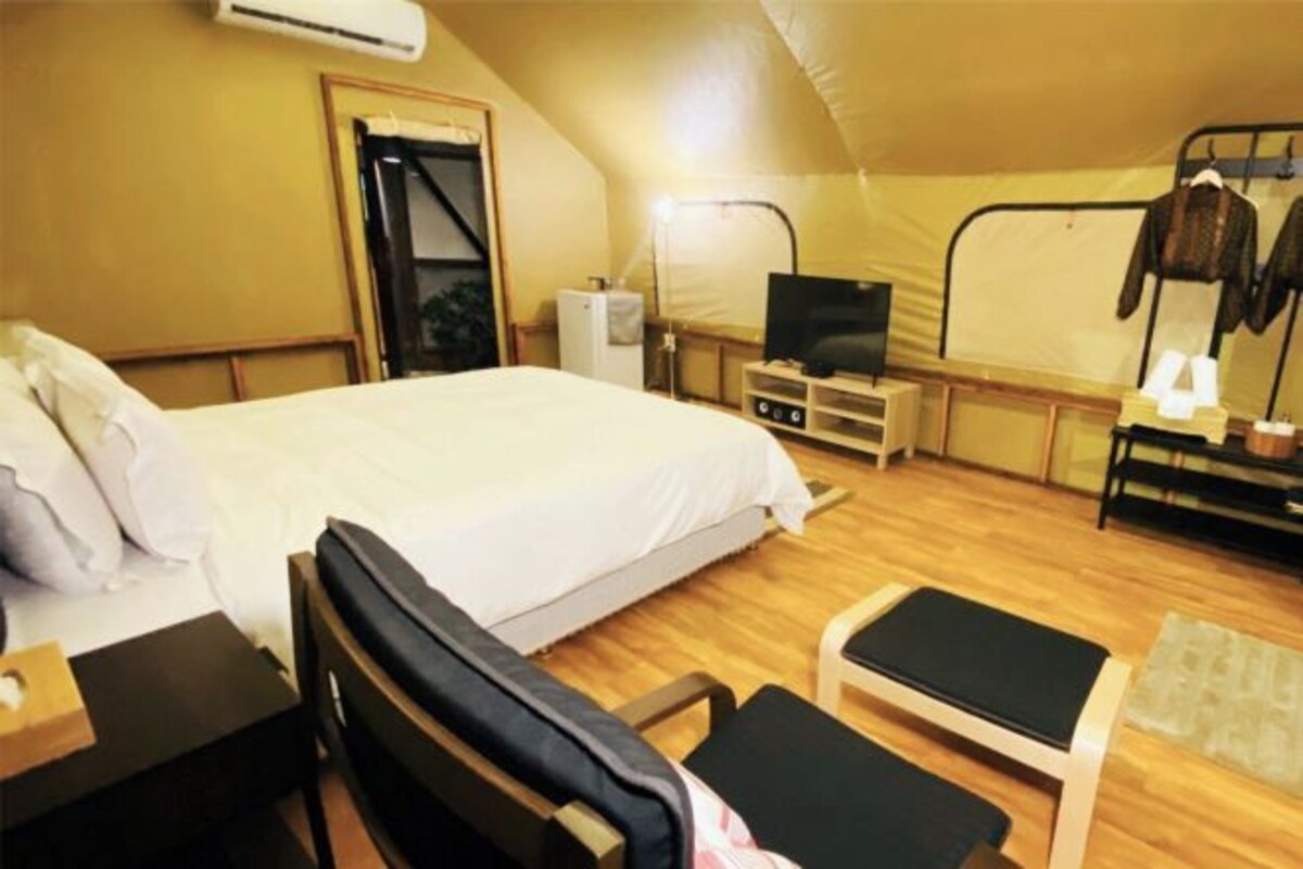 A tent-style room with a bed, a desk, a chair, a TV, and a coat rack.