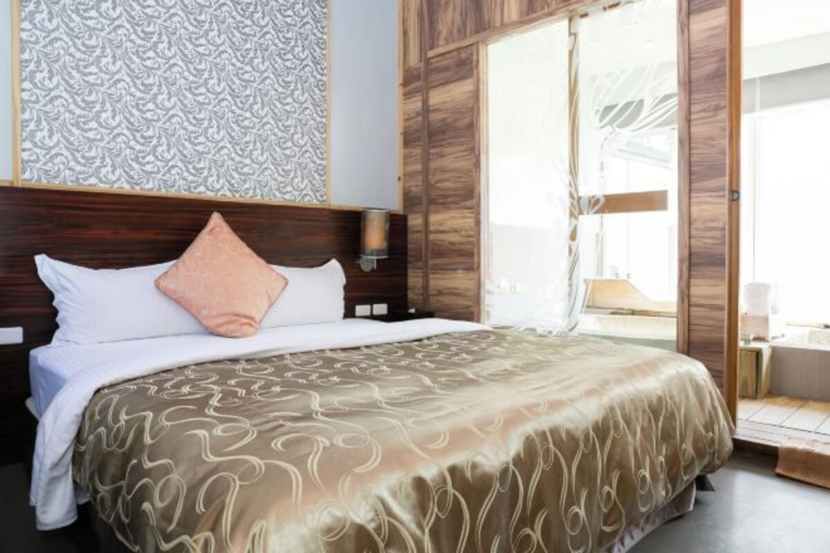A hotel room with a large bed, a wooden headboard, a patterned wall, and a view through a glass door.