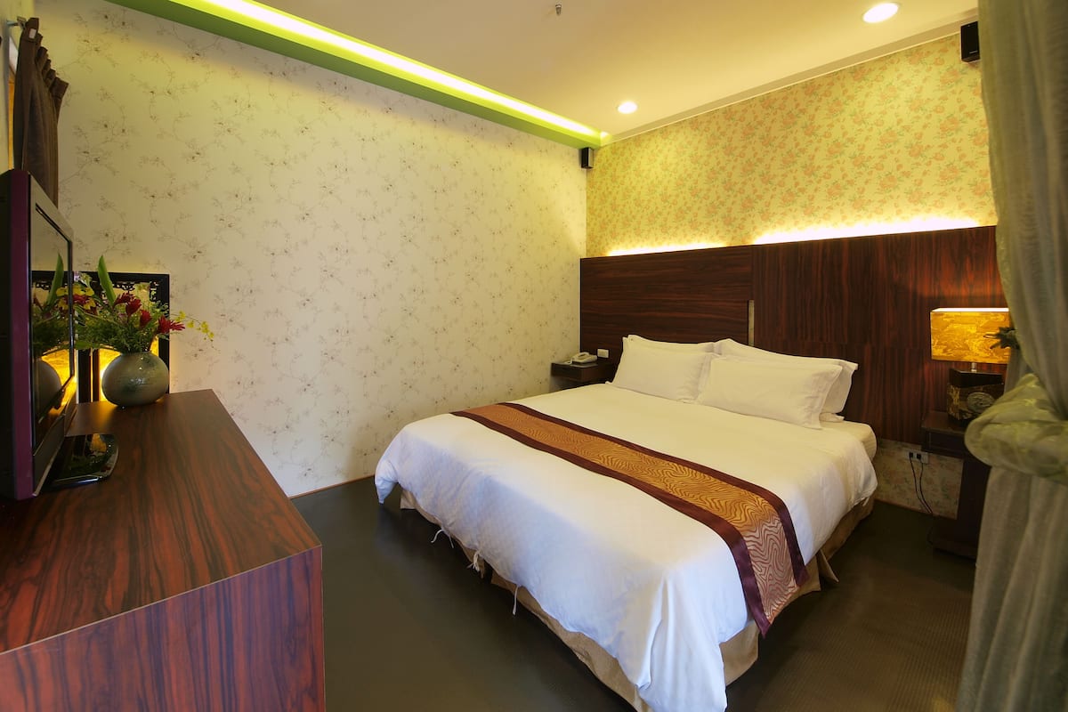 Une chambre d’hôtel avec un grand lit, une table de chevet et un bureau agrémenté d’un vase de fleurs.