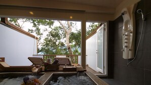 A spa area with a hot tub, wooden loungers, and a view of trees through large windows.