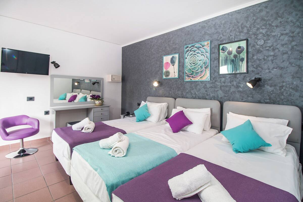 Una habitación de hotel con dos camas, un tocador, un televisor y obras de arte en la pared.