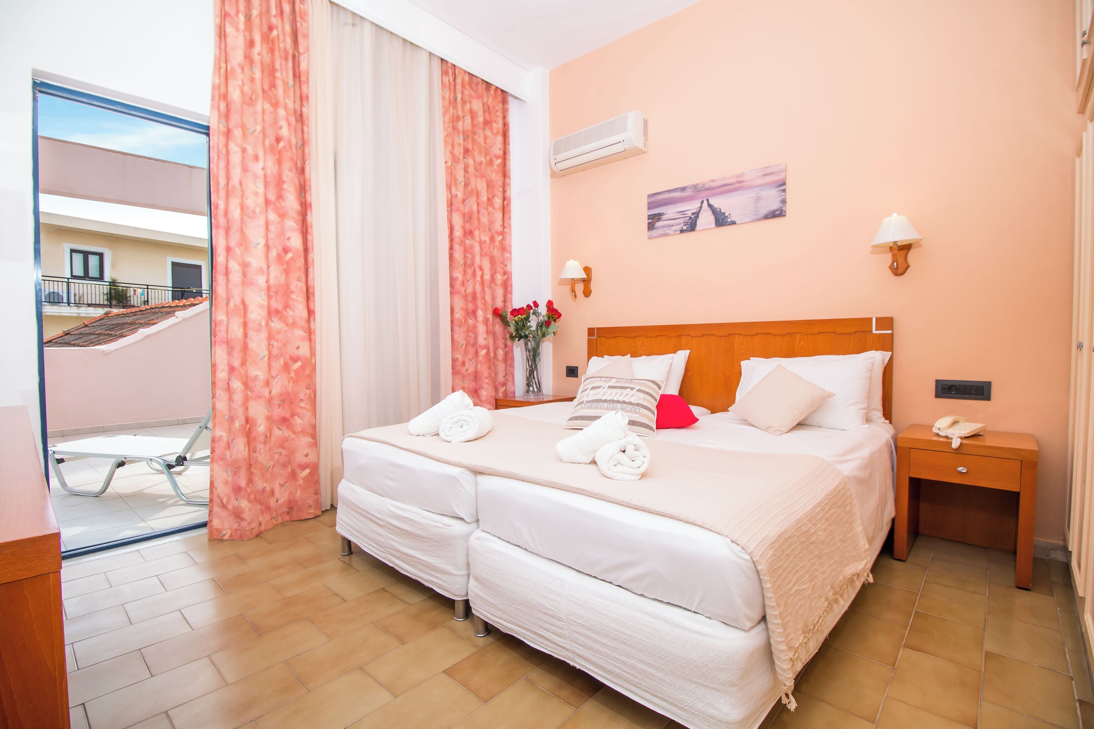 A hotel room with a bed, a nightstand, a vase with flowers, and a view of the outside balcony.