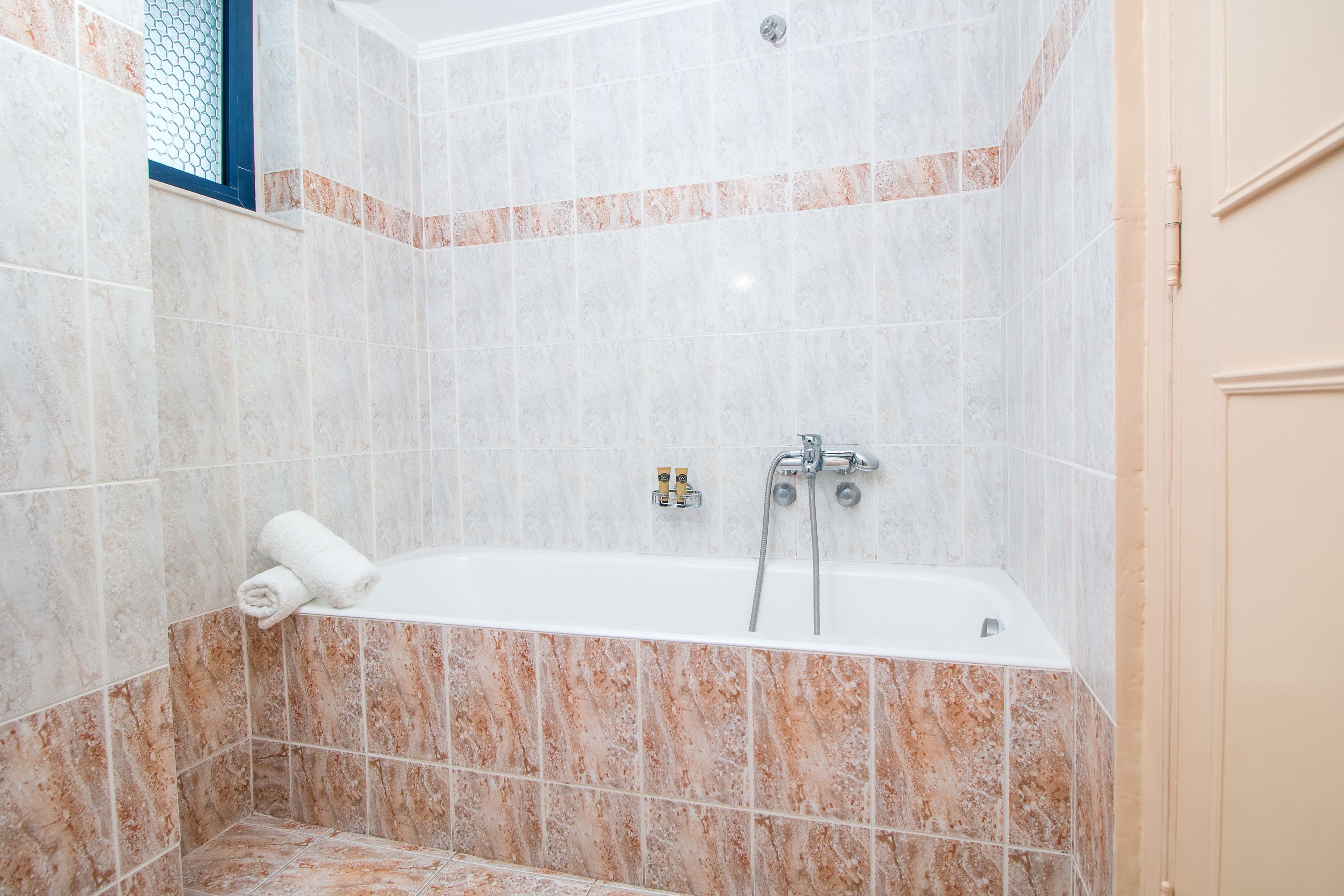 A bathroom with a bathtub, a window with a metal screen, and a towel on the edge.