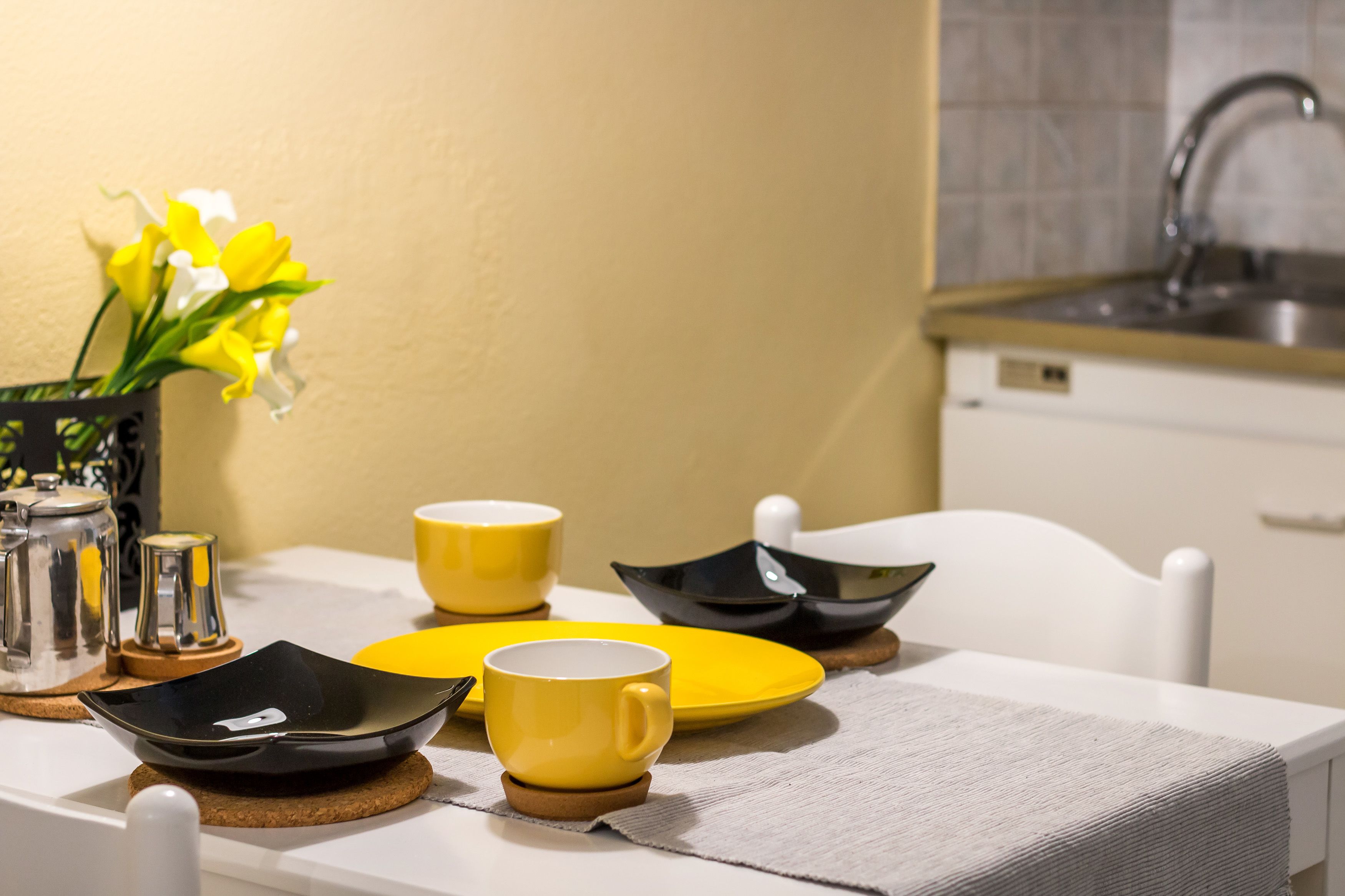 Ein Esstisch mit gelb-schwarzen Geschirr, einer gelben Tasse und einer Vase mit gelben Blumen.
