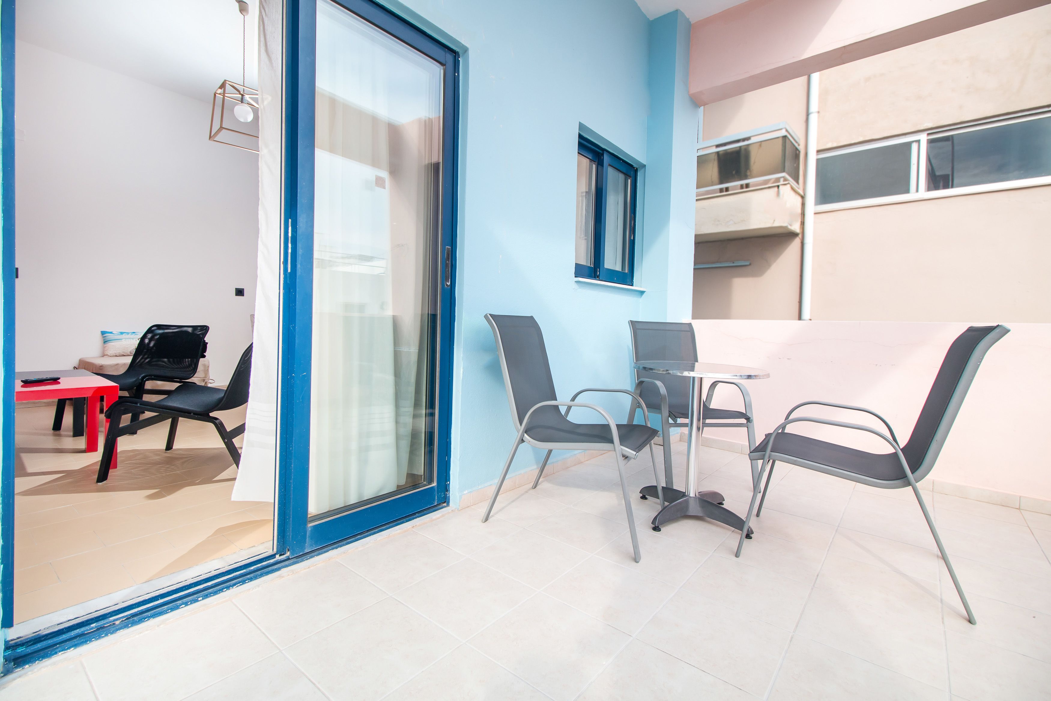 A modern room with a glass door leading to an outdoor area, a small table with chairs, and a window with a view of a building.