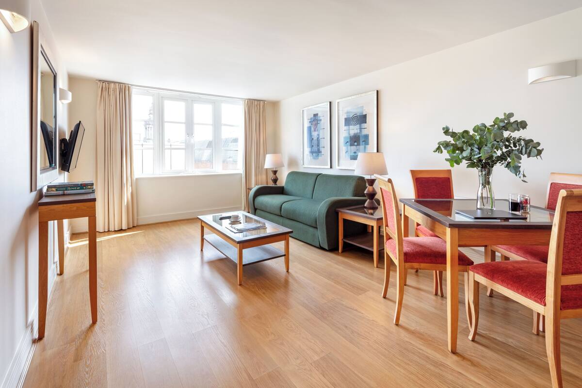 A modern living room with a sofa, a dining table with chairs, a coffee table, and a large window with curtains.