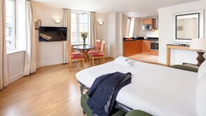Habitación de hotel con cama, televisión, mesa de comedor con sillas y kitchenette.