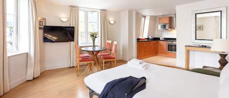 A hotel room with a bed, a TV, a dining table with chairs, and a kitchenette.