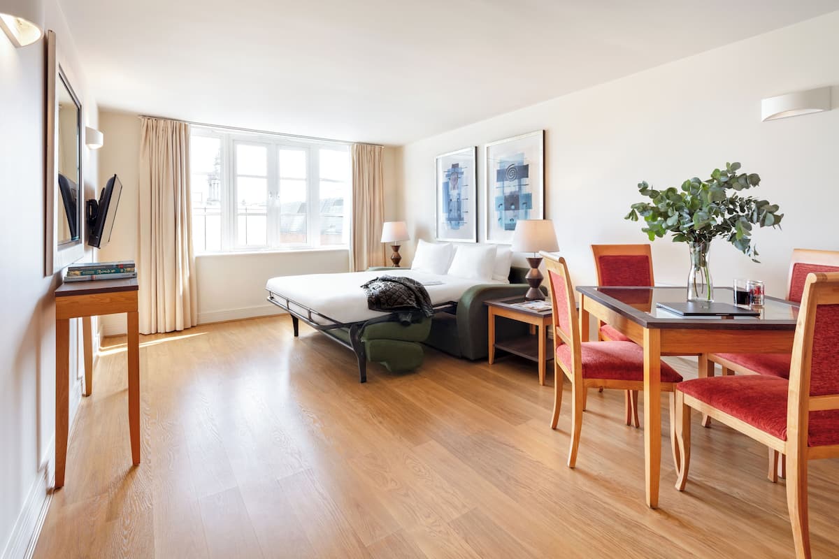 A hotel room with a bed, a desk, and a dining table with chairs.