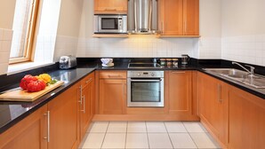 Una cocina moderna con armarios de madera, una campana extractora de acero inoxidable, un horno empotrado y una encimera negra.