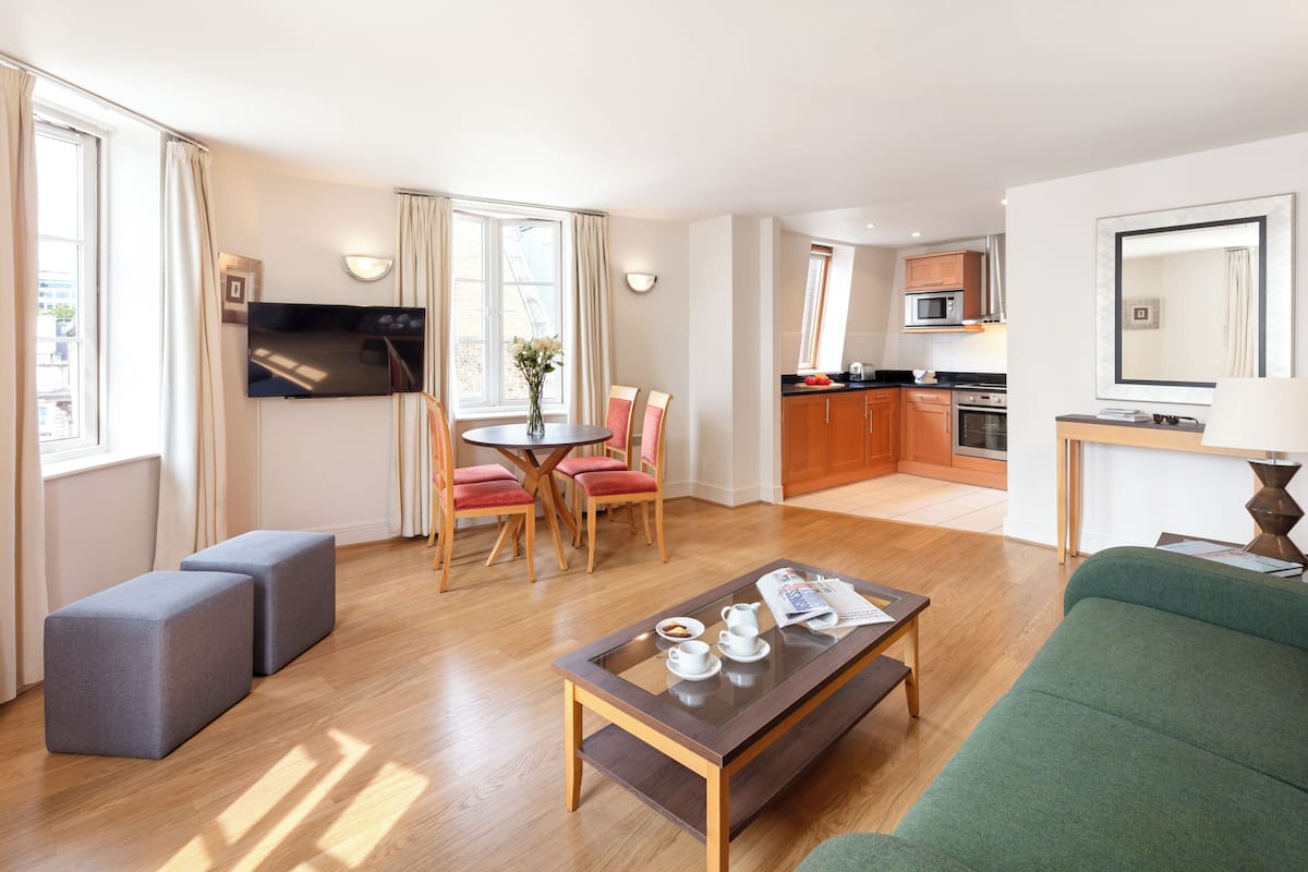 A modern hotel room with a dining area, kitchenette, and a green sofa.