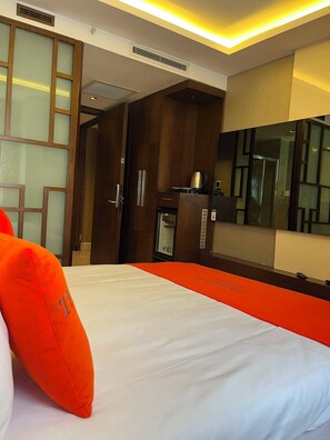 A hotel room with a bed, a wardrobe, a minibar, and a large mirror.