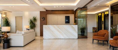 A modern hotel lobby with a reception desk, seating area, and a glass partition.