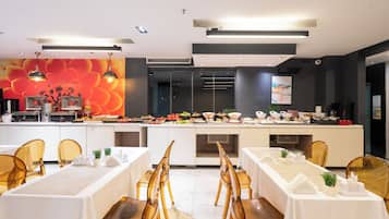 Uma área de refeições moderna com serviço de buffet, toalhas de mesa brancas e cadeiras de vidro transparente.