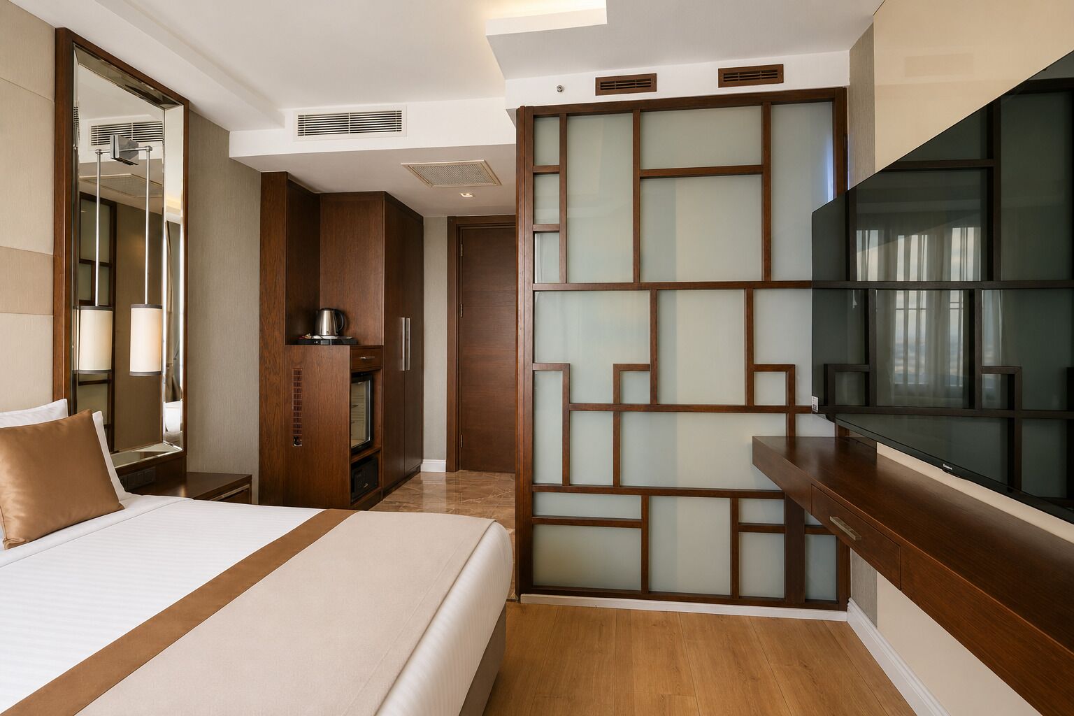 Una habitación de hotel con cama, televisión, aparador de madera y un biombo decorativo.