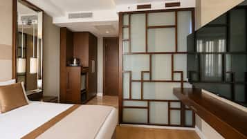 Quarto de hotel com cama, televisão, armário de madeira e um biombô decorativo.
