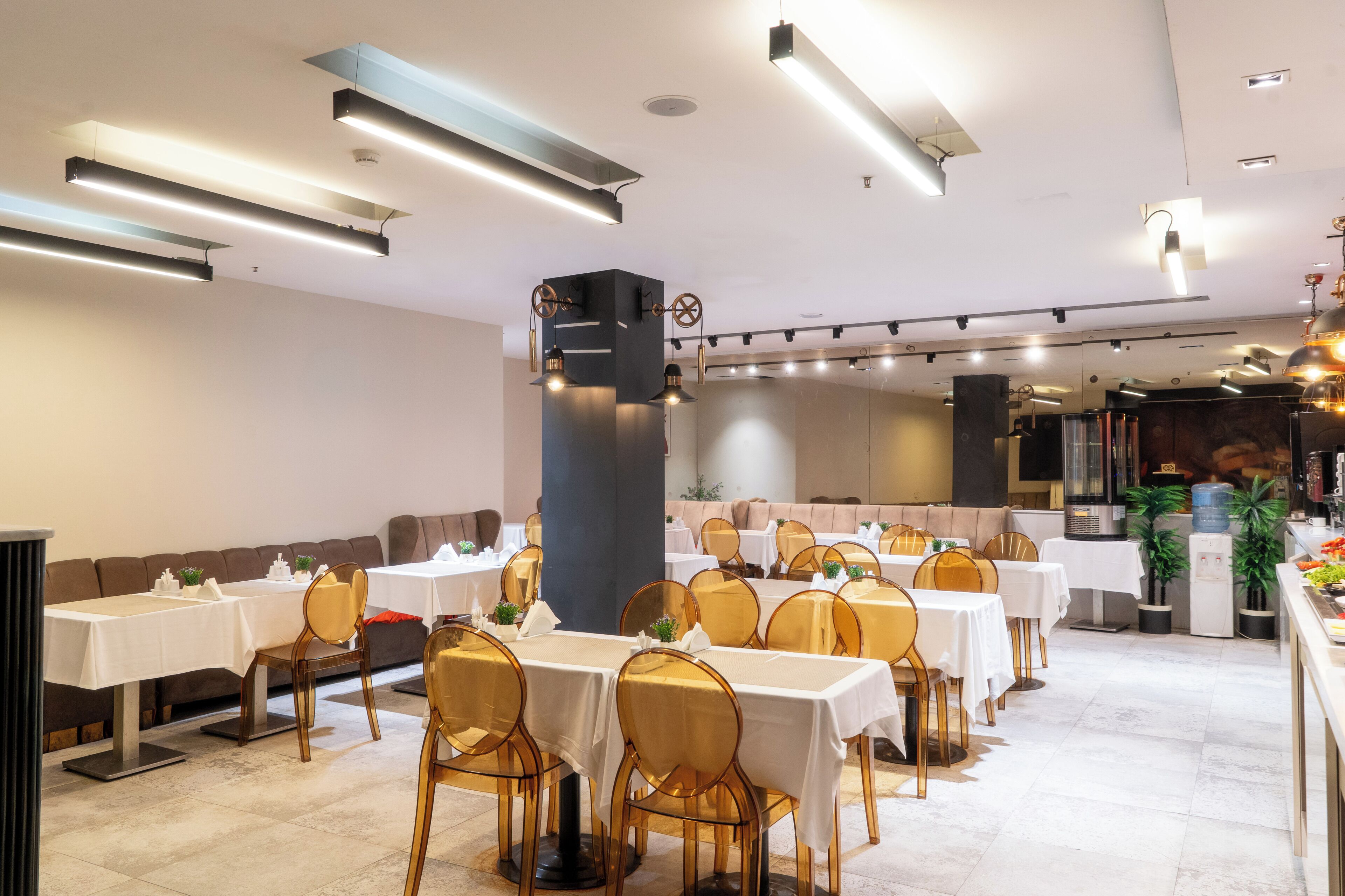 Um restaurante com várias mesas e cadeiras, um pilar grande e um dispensador de água.