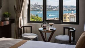 A hotel room with a bed, two chairs, a small table with a coffee maker and cup, and a window with a view of a cityscape and water. - The Biancho Hotel Pera (Istanbul)