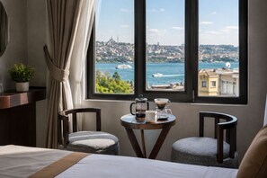 A hotel room with a bed, two chairs, a small table with a coffee maker and cup, and a window with a view of a cityscape and water. - The Biancho Hotel Pera (Istanbul)