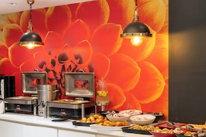 A buffet setup with various food stations, a coffee machine, and a decorative wall with a floral pattern.