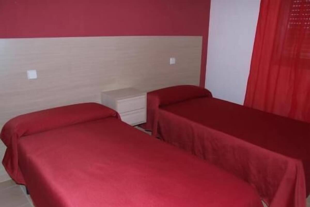 A room with two single beds, each with a red bedspread, a small bedside table, and a wall-mounted light.