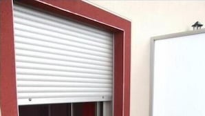 Una porta de garatge tancada amb un marc vermell, una porta corredissa de vidre i una pissarra penjada a la paret.