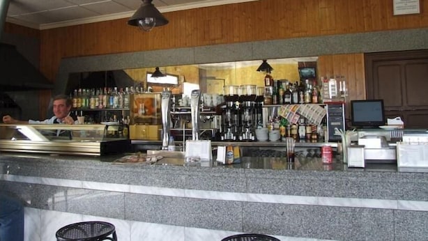 Zona de bar amb taulell, prestatges plens de garrafes, televisió i paret de fusta.