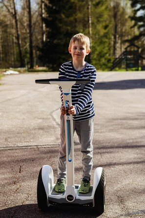 A person riding a Segway on a paved path surrounded by trees.