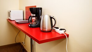 A red table with a coffee maker, a kettle, and a microwave.