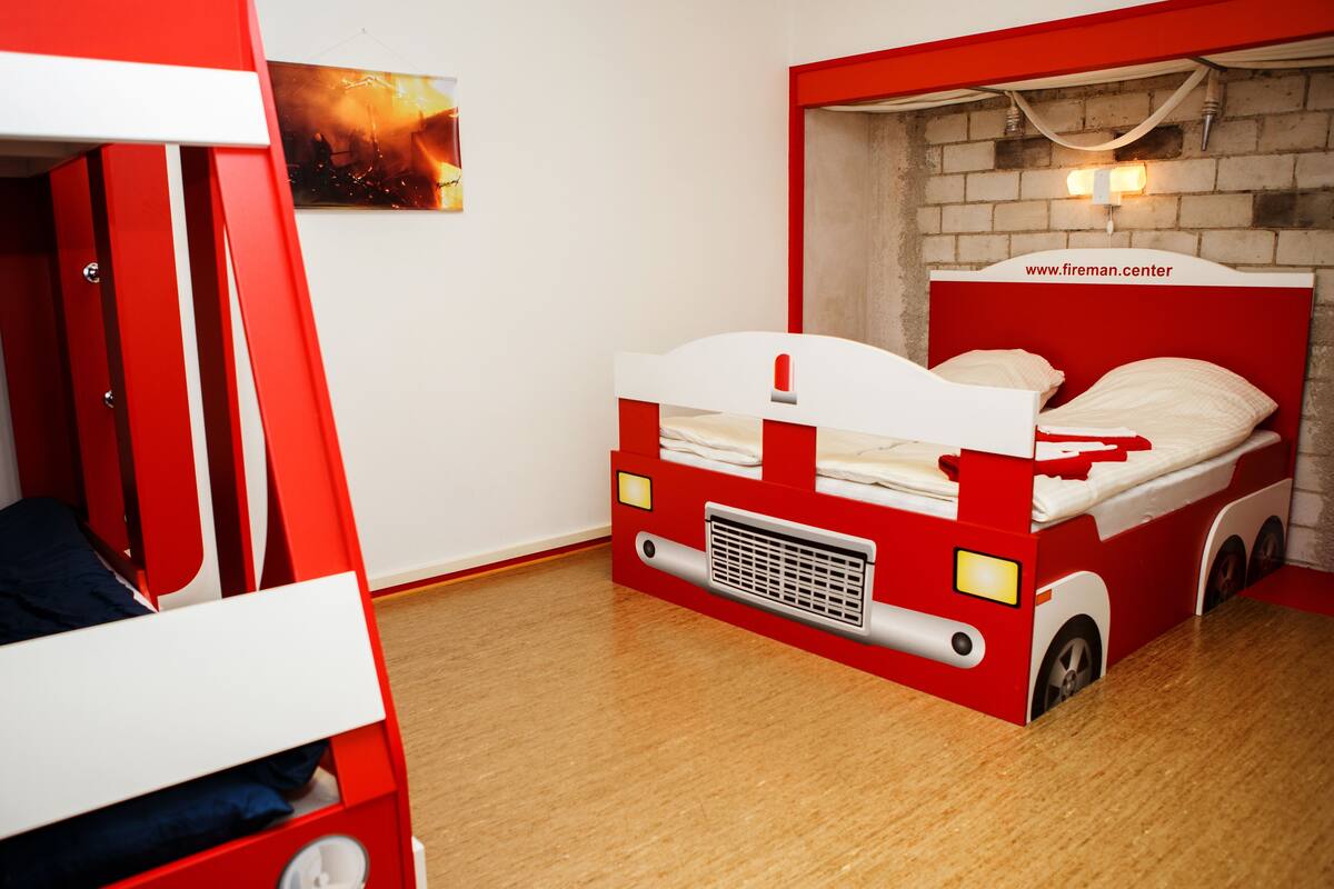A child's bedroom with a red and white bunk bed, a small heater, and a brick wall.