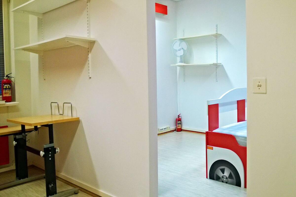 A room with a bunk bed, a desk, and shelving units.
