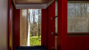 A narrow hallway with a bed at the end, a door leading outside, and a window with blinds.