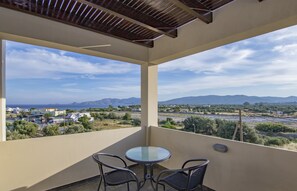 A balcony with a glass table and chairs, offering a view of a coastal landscape with mountains and buildings. - Haraki Villas (Rhodes)